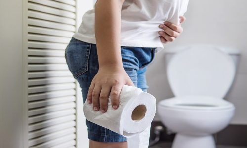 Asian boy sitting on toilet bowl holding tissue paper  - health problem concept
